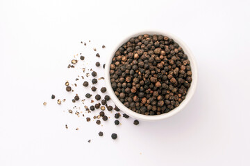 Black pepper or peppercorns in ceramic bowl with broken isolated on white background , top view , flat lay.