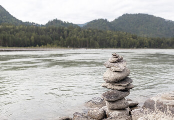 A pyramid of bare stones stacked on top of each other. Stones stacked in the shape of a pyramid on the riverbank against the background of mountains as balance and balance in nature, Zen, Buddhism.