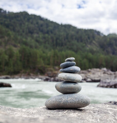 A pyramid of bare stones stacked on top of each other. Stones stacked in the shape of a pyramid on the riverbank against the background of mountains as balance and balance in nature, Zen, Buddhism.
