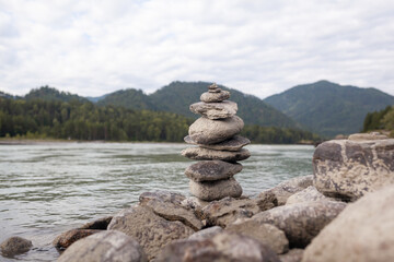 A pyramid of bare stones stacked on top of each other. Stones stacked in the shape of a pyramid on the riverbank against the background of mountains as balance and balance in nature, Zen, Buddhism.