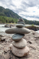 A pyramid of bare stones stacked on top of each other. Stones stacked in the shape of a pyramid on the riverbank against the background of mountains as balance and balance in nature, Zen, Buddhism.