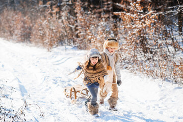 Fototapeta na wymiar Two happy children are running on snowy road in winter. Family on winter walk.