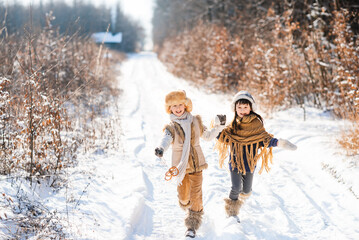 Two happy children are running on a snowy road in winter. Family on a winter walk.