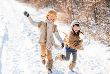 Cheerful children play together in snow in winter. Children run along snowy road.