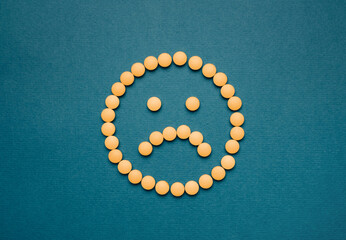 The pills are laid out on a blue background in the form of a sad emoticon. Antidepressants concept or headache.