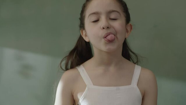 A girl's mouth is a genetic trait inherited from her parents, with her tongue curling into a U-shaped macro. Close-up view of a little schoolgirl girl sticking out her tongue and raising her sides up.
