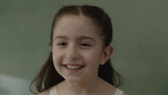 Little girl squinting her eyes having fun. Cute, funny and naughty little girl squinting in front of blackboard at school, smiling and looking at camera