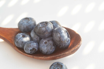 Closeup blueberry in a wooden spoon and green leaves. Blur and selective focus.