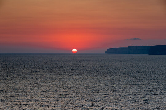 A colourful sunset over the cliffs of Paradis bay in Malta with a view on the Island of Gozo in the Mediterranean Sea. In summer the countries around the Mediterranean enjoy every evening these sunset