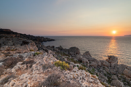 A colourful sunset over the cliffs of Paradis bay in Malta with a view on the Island of Gozo in the Mediterranean Sea. In summer the countries around the Mediterranean enjoy every evening these sunset