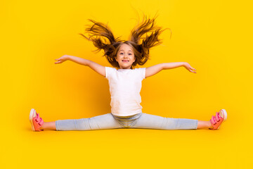 Full length photo of sweet charming schoolgirl dressed white t-shirt sitting split legs flying hair isolated yellow color background - obrazy, fototapety, plakaty