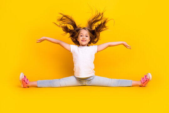 Full length photo of sweet charming schoolgirl dressed white t-shirt sitting split legs flying hair isolated yellow color background