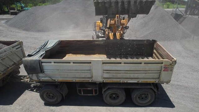 Sand loaders are shoveling rocks into dump trucks.
