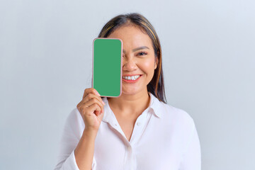 Smiling young Asian woman covering half face with blank screen mobile phone, recommending mobile app isolated over white background
