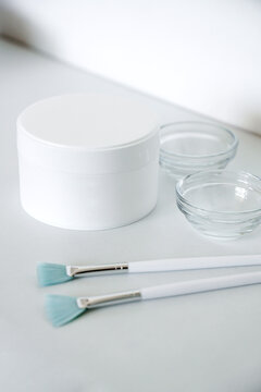 Skin care products at beauty salon mockup. Closeup shot of white plastic jar with face cream, glass bowl and peeling brushes on grey. Vertical photo