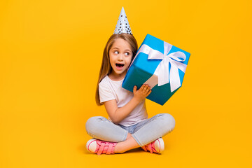 Full length photo of impressed suspicious school girl wear white t-shirt birthday cap listening inside present isolated yellow color background