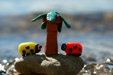 Obraz premium Two toy ladybugs and a palm tree on the background of the river. Bright sunny day. Vacation at the sea.