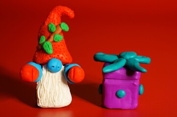 A toy gnome with a gift on a red background. New Year and Christmas. Fabulous scenery.