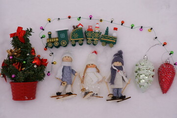 Toy angels on skis, decorated with a scarf and a hat. Next to the train with gifts and a Christmas tree. Figurines in the winter forest. 