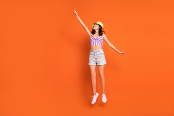 Full length photo of positive charming lady purple swimwear jumping high pointing empty space isolated orange color background