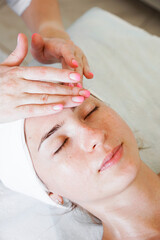 Pretty yanog woman receiving face massage, closeup photo. Vertical photo. Beautician's office