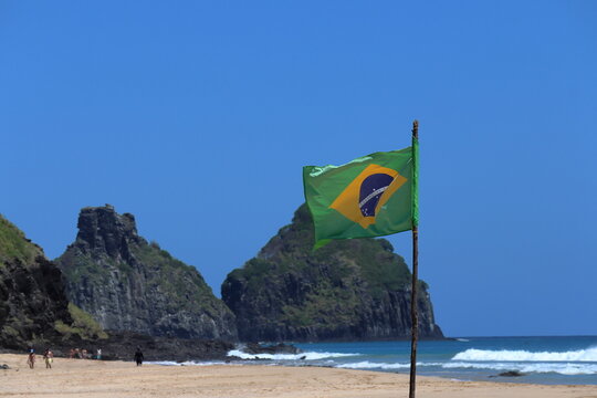 Brazilian flag waving  with Two Brothers cliff with the in the background at Bode beach, Fernando de Noronha, Pernambuco, Brazil, August, 2022