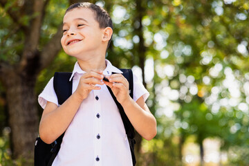 Happy laughing smiling boy student by yellow bus on first September day. Hard of hearing child kid eating apple fruit at school yard outdoors. Education and back to school in Autumn Fall