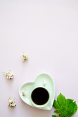 Obraz na płótnie Canvas Flatlay with a white cup of coffee and a saucer in the shape of a heart in the lower corner of a light purple background, large copyspace and chestnut flowers and leaf, multi-colored, light, delicate