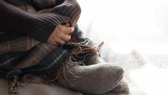 Autumn winter season warm knitted socks and a woolen blanket. A woman Is resting at home on a winter evening in a cold apartment
