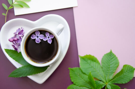 close-up flatlay diagonal Mockup of white cards and a pink envelope on a dark purple background Copyspace with leaves and lilac flowers with a coffee cup and heart-shaped saucer - Powered by Adobe