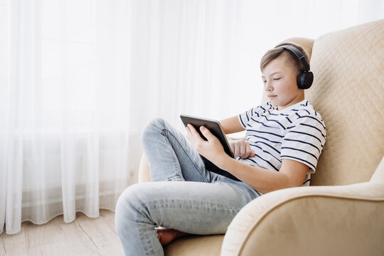 Teenage boy in wireless headphone using tablet having video chat on internet online at home. Child watching movie, playing video game. Social media concept. Online education. Distance learning