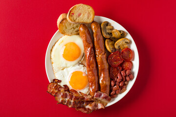 Plate with English breakfast on red background.