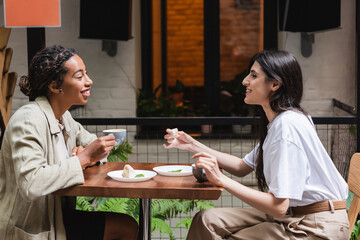 Side view of multiethnic friends talking near coffee and desserts in outdoor cafe