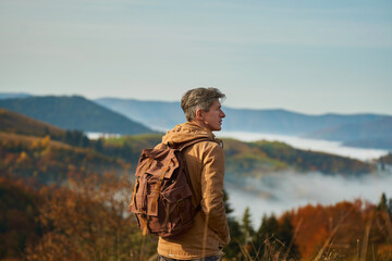 Outdoors portrait adult man with backpack admiring beautiful landscape over mountains and clouds,...