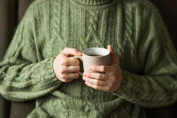 Married man wearing green knitted woolen sweater holding hot cup of tea in the cold autumn or...