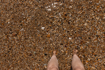 A close up view of a pair of feet buried into the sand-pebbles in the celar ocean water