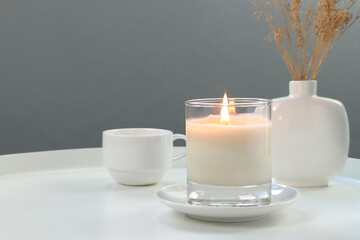 luxury lighting aromatic scented candle is on white metal table with ceramic vase and a coffee cup to creat relax ambient in the livingroom with background of nice grey cement wall on Valentine day