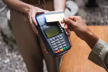 Cropped view of waitress holding payment terminal near african american client with credit card on...