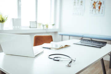 Empty Doctor's Office With Examination Table And Doctor's Desk. Stethoscope, prescription medical form lying on a table with pc computer. Medicine or pharmacy concept. 