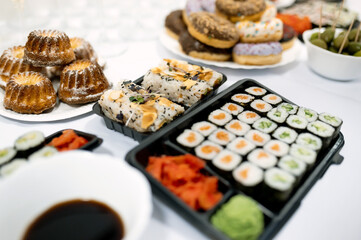 sushi of different types, muffins, donuts lie on the table