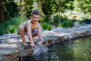 Funny little boy coming out from garden pond with splashing around him. Summer holiday, vacation concept.
