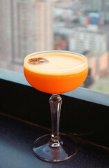 A glass of vibrant orange cocktail at rooftop terrace with blurry urban view in the backdrop