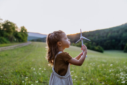 Little girl standing in nature with model of wind turbine. Concept of ecology future and renewable resources.