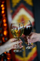 glasses of red and white wine in female hands on the background of an ornamented wall
