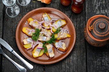 herring fillet on potatoes with onions and greens in a clay plate
