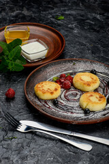 breakfast cheesecakes in a clay plate with jam and honey on a dark table vertical photo
