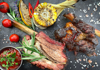 Grilled beef ribs on black slate board with corn and sauce. Top view, close up