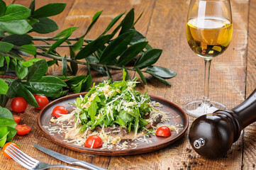 Georgian salad with arugula cheese and meat in a plate with pomegranate seeds on the table with a glass of wine

