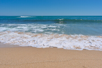 Clear emerald green sea with white foam and clean sandy beach