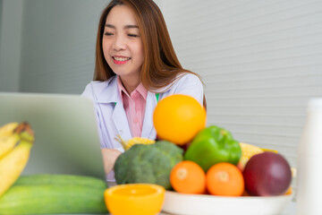 Fototapeta premium Portrait of Asian smiling female nutritionist typing on laptop computer for balanced corrective diet plan for patient or weight loss advice. Concept of healthy lifestyle, healthy food, dieting